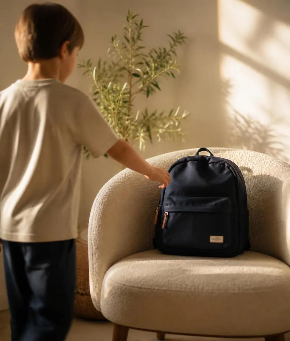 A child reaching for a navy school backpack in warm morning light