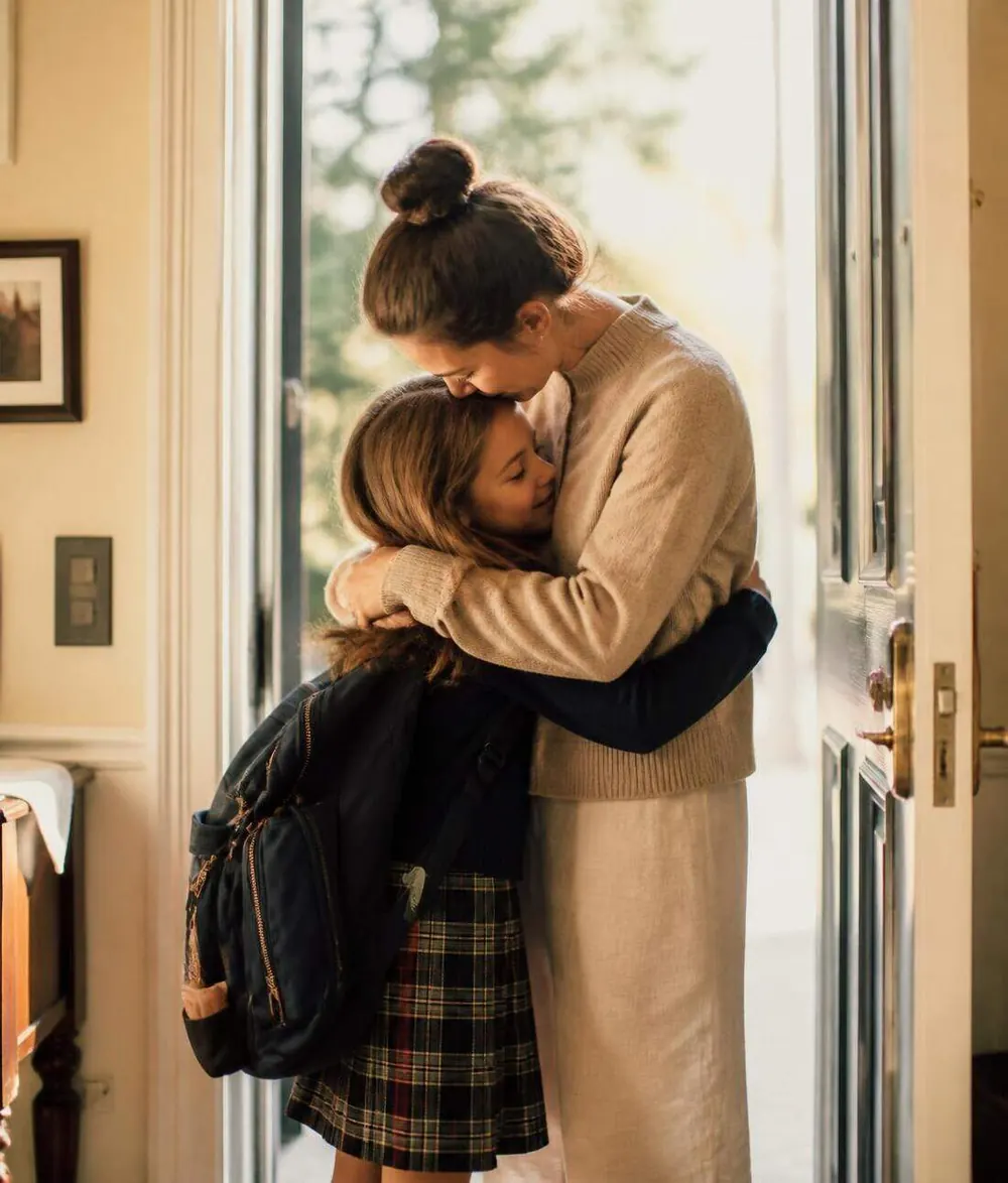 A mother hugging her child goodbye at the doorway